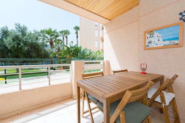 Una mesa y sillas de madera en un balcón con vistas a palmeras y un edificio.