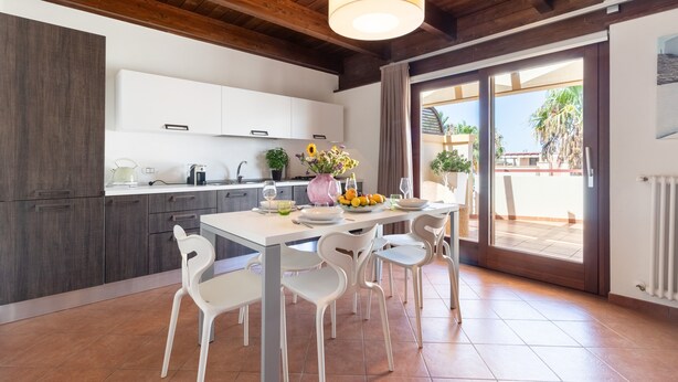 Una cucina moderna con mobili bianchi, un tavolo da pranzo con sedie e vista all'esterno tramite una porta in vetro.