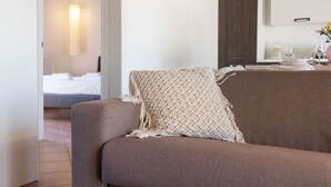 Un soggiorno moderno con divano, un cuscino decorativo, una zona pranzo con tavolo e sedie, e una cucina sullo sfondo.