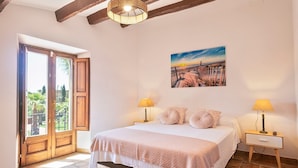 A bedroom with a bed, two bedside lamps, a painting, and a wooden door.