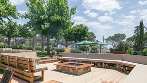 An outdoor patio with a stone fire pit, wooden seating, and a green umbrella.