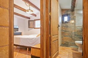 Une chambre à coucher avec un lit, une table de chevet, une télévision et une poutre en bois au plafond.