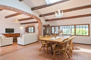A spacious living area with a dining table, wicker chairs, a sofa, a television, and a fireplace.
