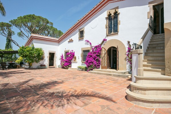 A white building with a tiled courtyard, a staircase, and a door.