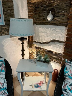 A stone wall, a white table with a floral tablecloth, a lamp, and a vase with flowers.