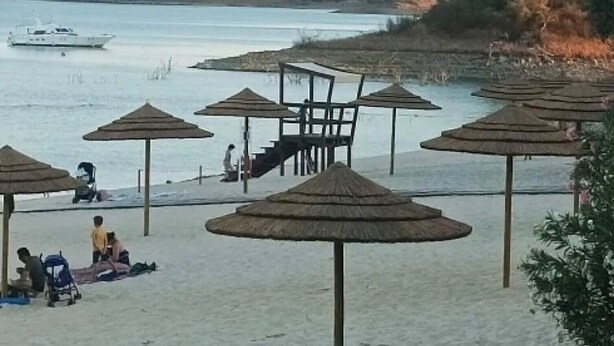 A beach with umbrellas, a chair, and a boat in the water.