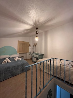 A bedroom with two beds, a desk, a hanging light fixture, and a window with blinds.