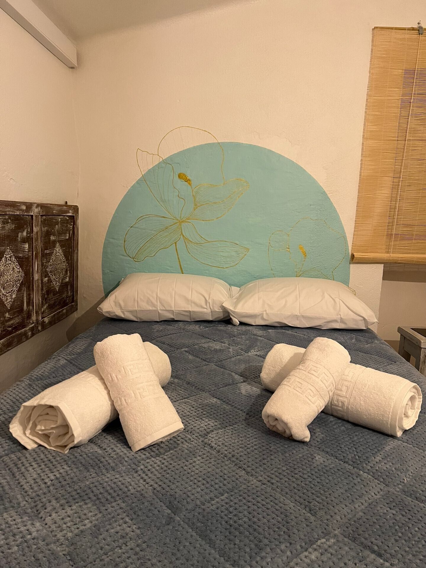 Un lit avec une couette bleue, deux oreillers blancs et des serviettes enroulées.