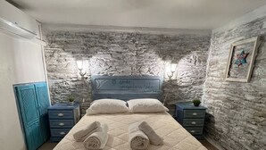 A bedroom with a stone wall, a bed with a quilt, two nightstands, a lamp, and a framed picture.