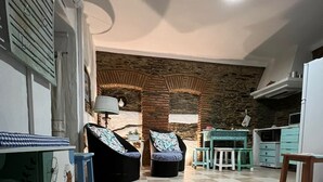 A room with a tiled floor, a sofa, a dining table, a lamp, and a kitchen area with a microwave.