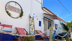 A coastal building with a sign reading 'CASA MESTRE DO LAU,' a wooden deck with lounge chairs, and potted plants.