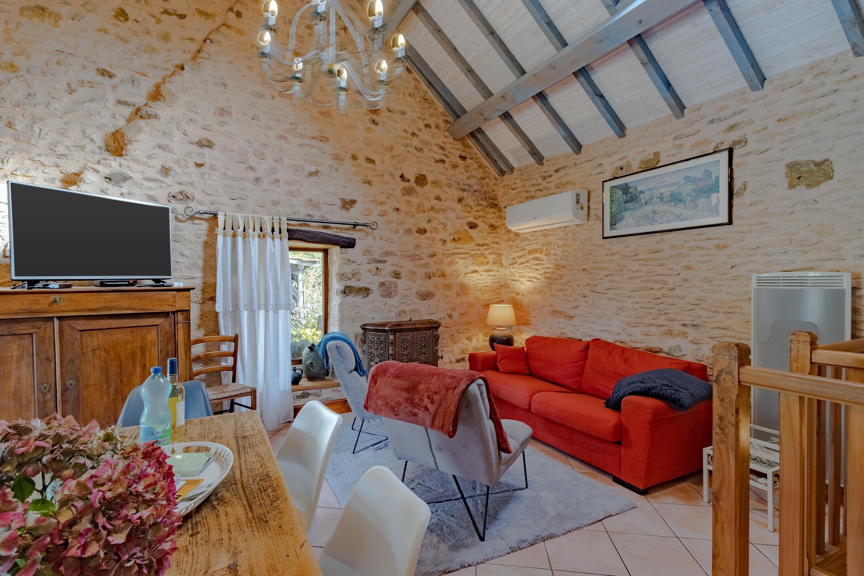Une pièce rustique aux murs de pierre, avec un canapé rouge, un téléviseur et un coin repas comprenant des chaises et une table.