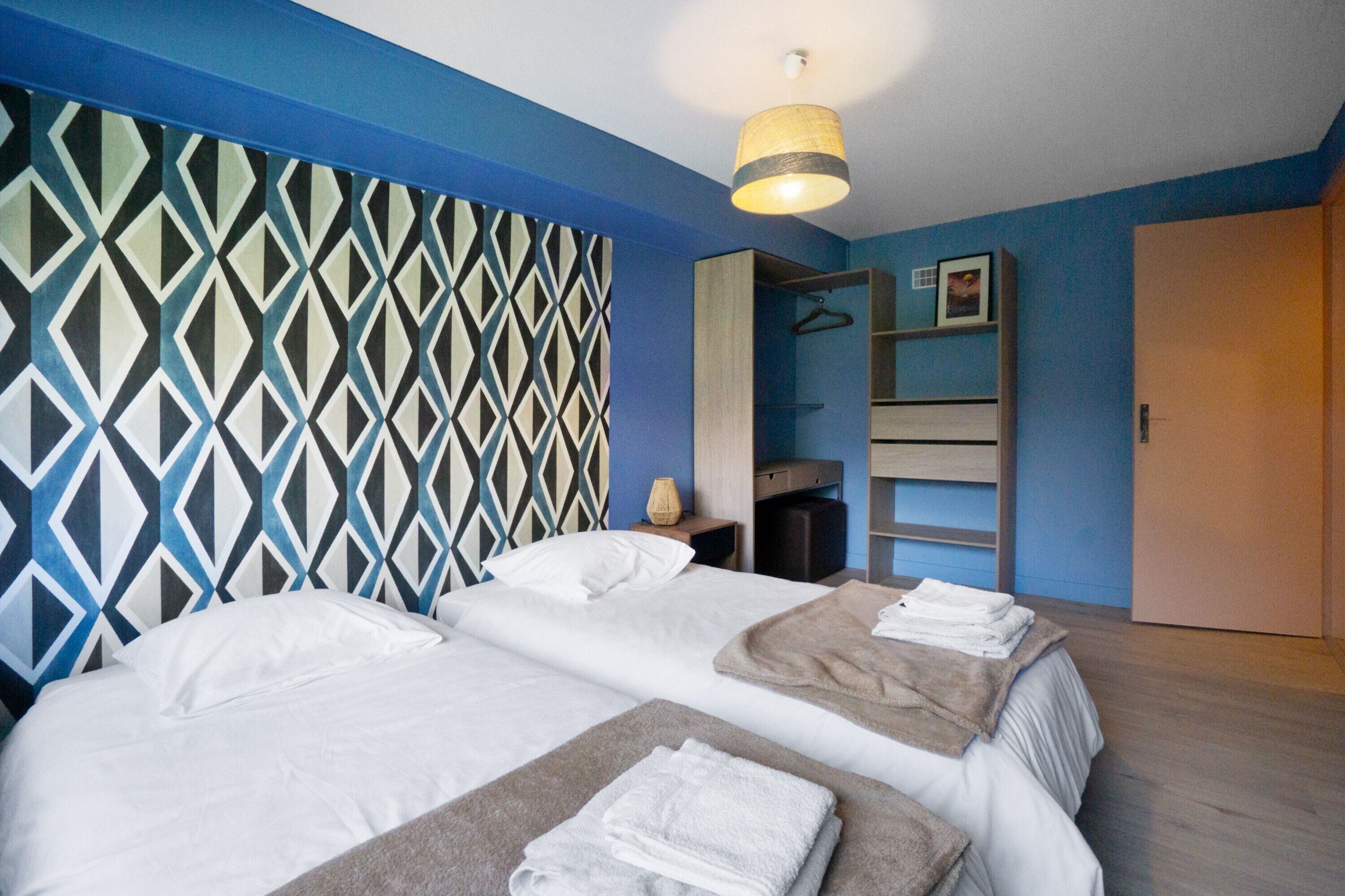 Ein Hotelzimmer mit zwei Betten, einem Schrank, einem Spiegel und einer Wand mit Muster.