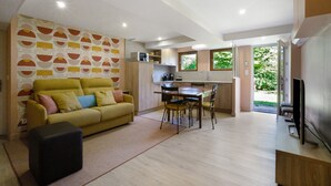 A living room with a sofa, a coffee table, a dining area with a table and chairs, a kitchen area, and a TV. - Apartment 'Chez Anna' with Mountain View, Wi-Fi and Air Conditioning (Saint-Jean-de-Maurienne)