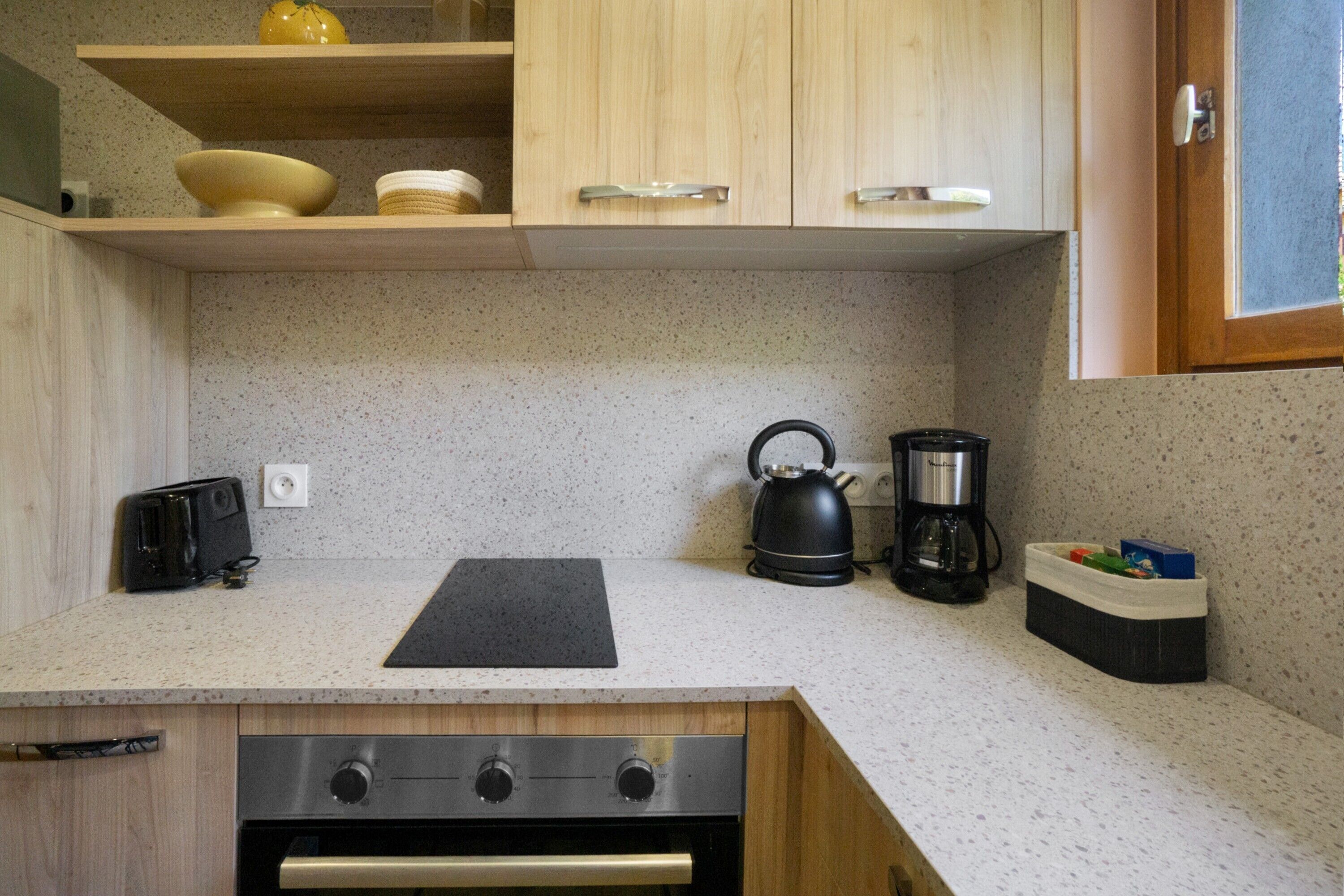 Eine kleine Küche mit Holzausstattung, Backofen, Wasserkocher und Kaffeemaschine.
