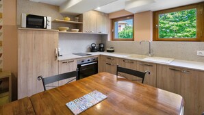 A compact kitchen with a wooden table, a microwave, a kettle, and a window with a view of greenery. - Apartment 'Chez Anna' with Mountain View, Wi-Fi and Air Conditioning (Saint-Jean-de-Maurienne)