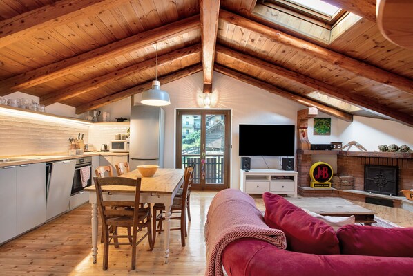 A cozy attic-style room with a wooden ceiling, a dining area, a sofa, and a fireplace.