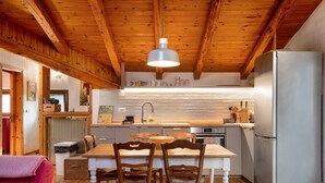 Een keuken met houten balken, een centraal eiland met stoelen, een koelkast en een hanglamp.