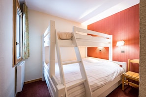 Un letto a castello con una scala, una sedia, un termosifone e una lampada fissata al muro.