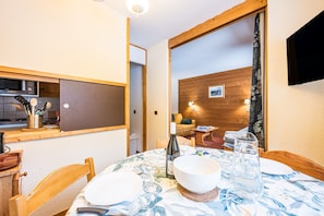 A dining area with a table set for two, a bottle of wine, and a pitcher of water. - Apartment 'Valmorel' with Mountain View and Balcony (Les Avanchers-Valmorel)