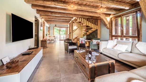 A spacious living area with a wooden ceiling, a staircase, a sofa, a coffee table, and a flat-screen TV. - Chalet 'La Glière De L'Etelley' with Mountain View, Private Terrace and Wi-Fi (Samoëns)
