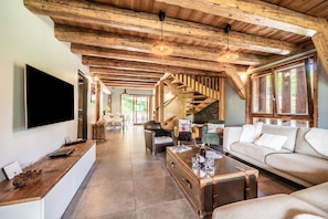 Ein geräumiger Wohnbereich mit Holzbalkendecke, einer Treppe, einem Sofa, einem Couchtisch und einem Flachbildfernseher.