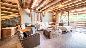 A spacious living area with a stone wall, wooden beams, a large sofa, a coffee table, and a view of the outdoors. - Chalet 'La Glière De L'Etelley' with Mountain View, Private Terrace and Wi-Fi (Samoëns)