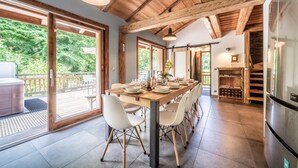 A dining area with a wooden table, white chairs, and a view of the outdoors. - Chalet 'La Glière De L'Etelley' with Mountain View, Private Terrace and Wi-Fi (Samoëns)