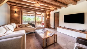 A modern living room with a wooden ceiling, a flat-screen TV, a sofa, a coffee table, and a large window. - Chalet 'La Glière De L'Etelley' with Mountain View, Private Terrace and Wi-Fi (Samoëns)