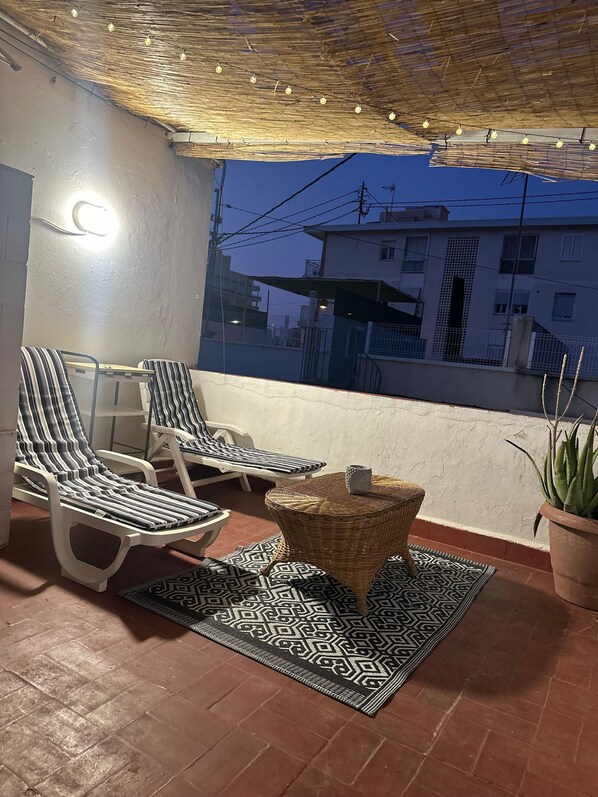 A balcony with two striped lounge chairs, a wicker table, and a patterned rug.
