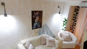 Une pièce avec un canapé blanc, un fauteuil blanc, une petite table, un tableau représentant un lapin et une plante.