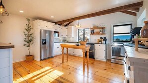 A kitchen with wooden flooring, white cabinets, a stainless steel refrigerator, a wooden dining table, and a large window with a view. - The View at Stoney Acres |  Pool + Hot Tub + Views (Mifflinburg)