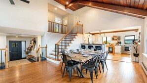 A spacious kitchen with modern appliances, a dining area with a wooden table and chairs, and a staircase leading to an upper level. - The View at Stoney Acres |  Pool + Hot Tub + Views (Mifflinburg)