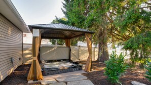 Een hottub onder een houten pergola, met stenen trappen ernaartoe, omgeven door bomen en een hek.