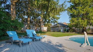 Een terras met Adirondack-stoelen, een zwembad en een huis op de achtergrond.
