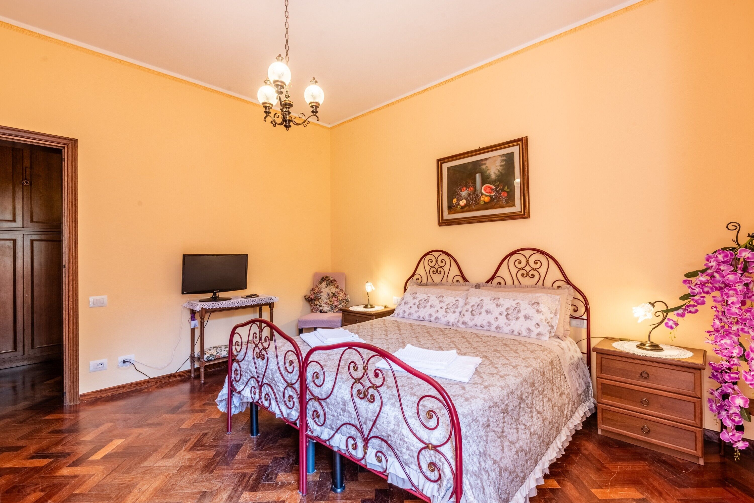 Een slaapkamer met een bed, een bureau, een stoel, een televisie, een nachtkastje, een lamp en een schilderij aan de muur.