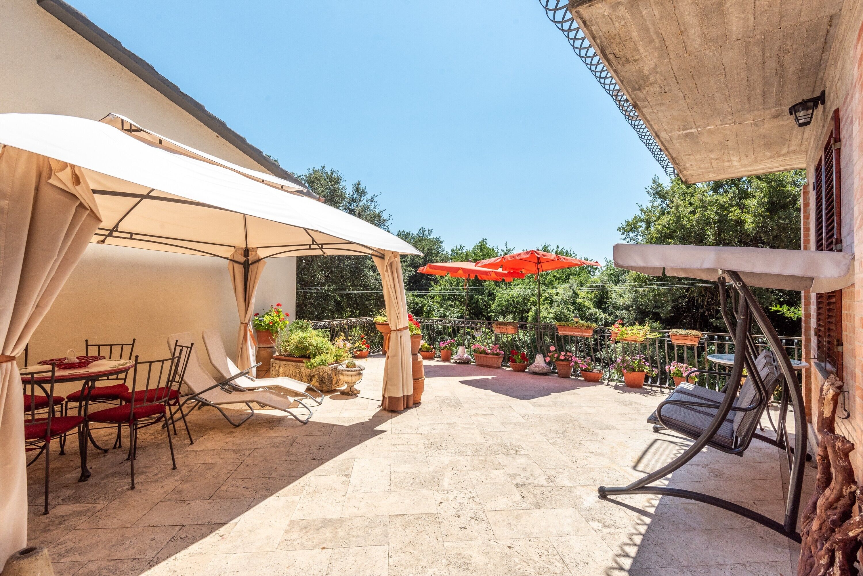 An outdoor patio with a covered dining area, lounge chairs, and potted plants.
