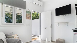 A modern living room with a sofa, a coffee table, a flat-screen TV mounted on the wall, and a door leading to another room.