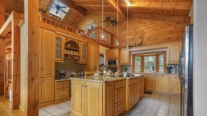 A spacious kitchen with wooden cabinets, a large island, and a view to the outside.