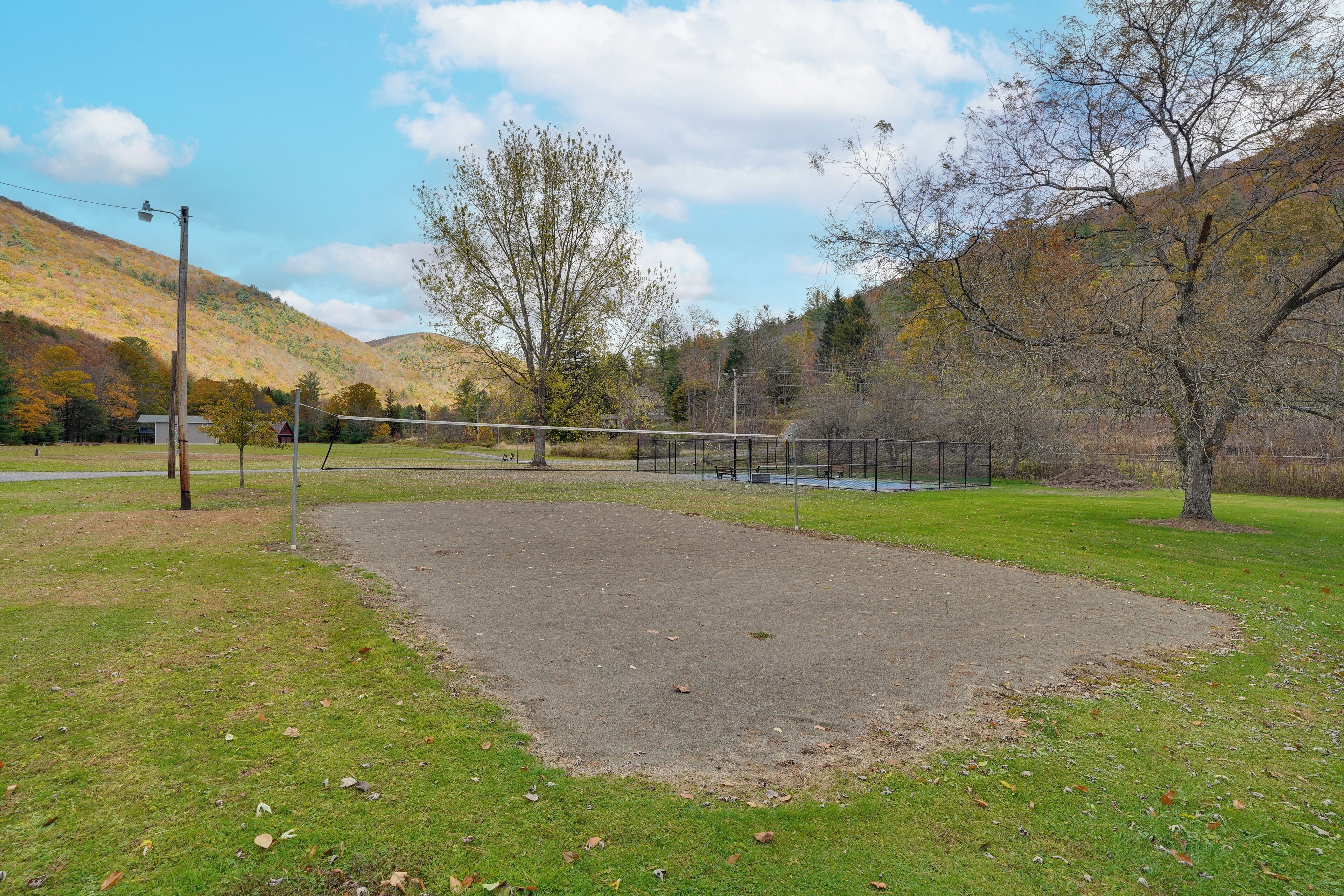 Un parc équipé d’un filet de volley-ball, d’une zone dallée et d’arbres.
