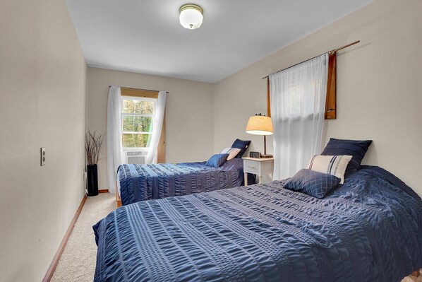 A bedroom with two beds, a nightstand, a lamp, and a window with curtains.