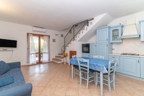 A living room with a sofa, a dining table with chairs, a kitchen with cabinets and a stove, and a staircase.