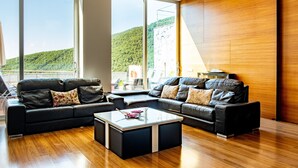 A modern living room with a large window, a black leather sofa, a glass coffee table, and wooden flooring. - Entregredos: Rural House in Sierra de Gredos with Pool and Jacuzzi (Guisando)