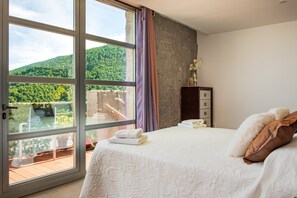 A bedroom with a large sliding glass door leading to a balcony, a bed with white bedding, a dresser, and a vase with flowers.