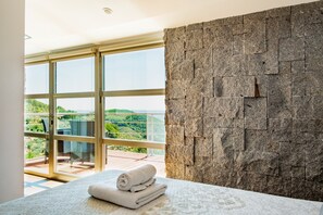 A bedroom with a large window, a stone wall, and a bed with rolled towels. - Entregredos: Rural House in Sierra de Gredos with Pool and Jacuzzi (Guisando)
