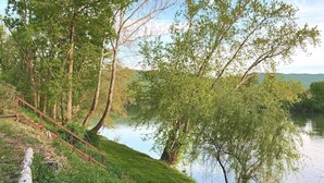 Une scène au bord de la rivière, avec un escalier en bois descendant jusqu’à l’eau, le tout entouré d’une végétation luxuriante et d’arbres.
