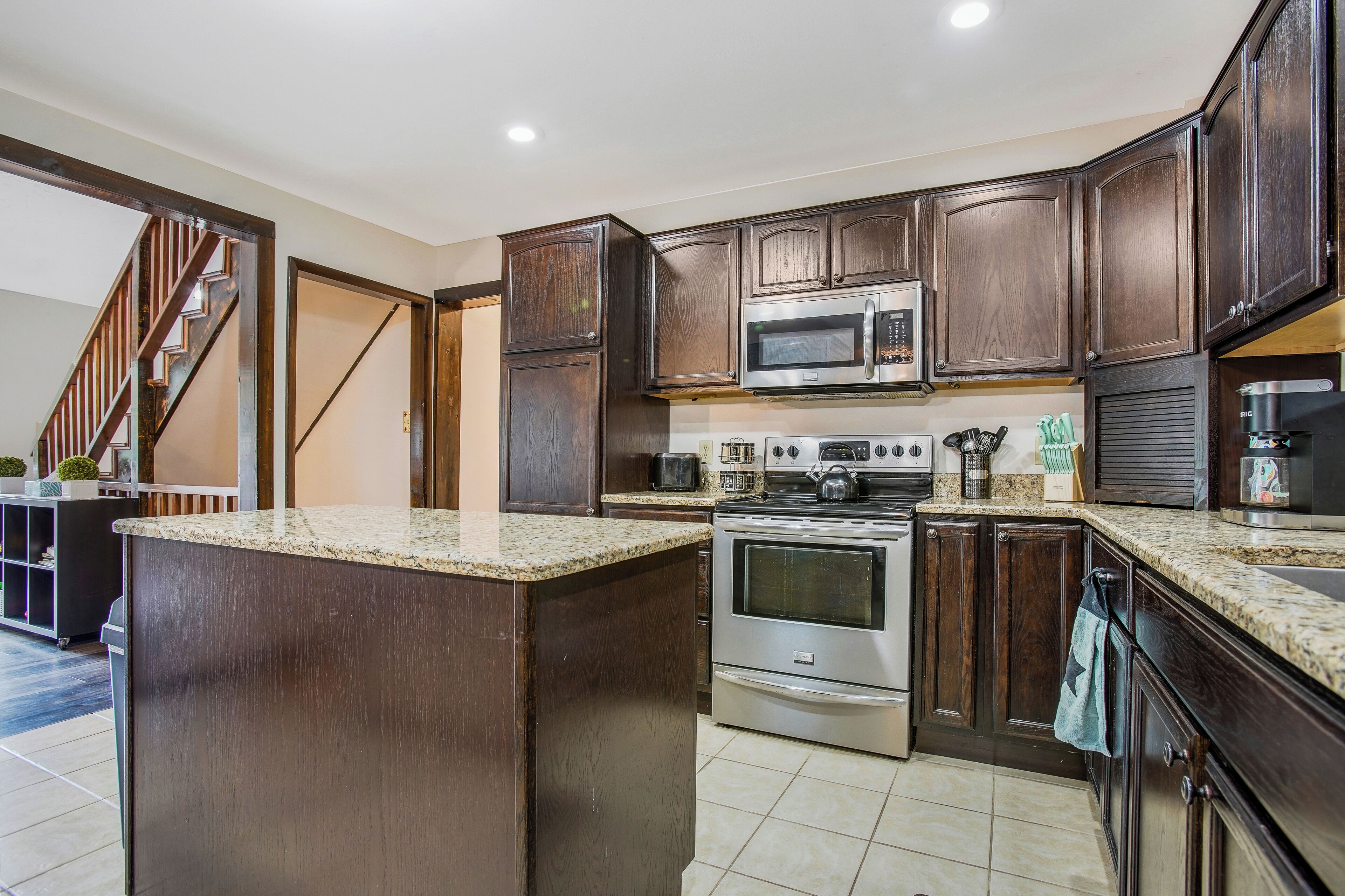 A kitchen with dark wood cabinets, granite countertops, stainless steel appliances, and a central island.