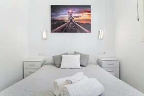 A bedroom with a bed, pillows, a nightstand, a wall-mounted picture of a lighthouse, and a power outlet.