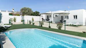 A swimming pool with a fenced area, white buildings, and a clear sky.