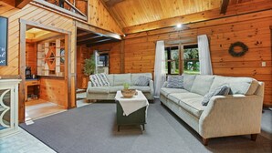 A cozy cabin interior with wooden walls, two sofas, a coffee table, and a kitchen area.